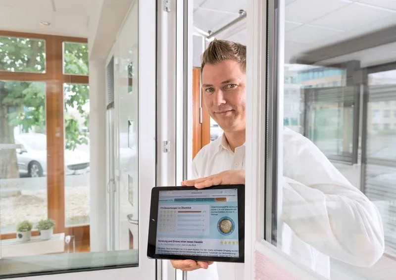 Mann hält ein Tablet mit einer Webseite über Fensterbewertungen. "GOLD-Wert" ist auf dem Bildschirm zu sehen.